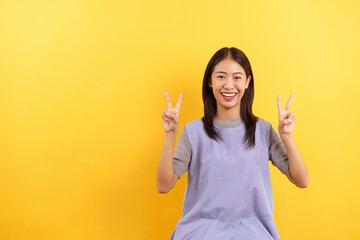 Young women making v sign with both hands and smile with empty space on isolated yellow background