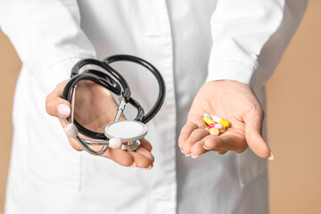 Young female doctor with stethoscope and pills on beige background