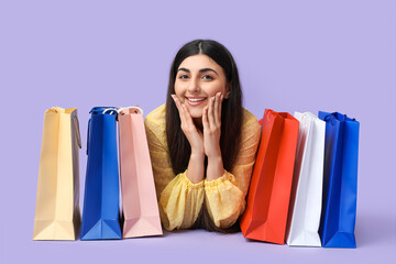 Happy smiling young woman with shopping bags lying on lilac background