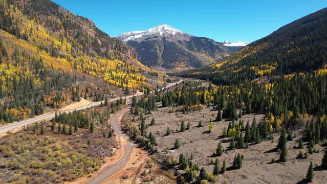 Aerial Yellow River Epic Landscape Colorado Million Dollar Highway Road Yellow Aspen Pine Trees Snow Top Mountains. Winding Yellow River Flying Backwards.
