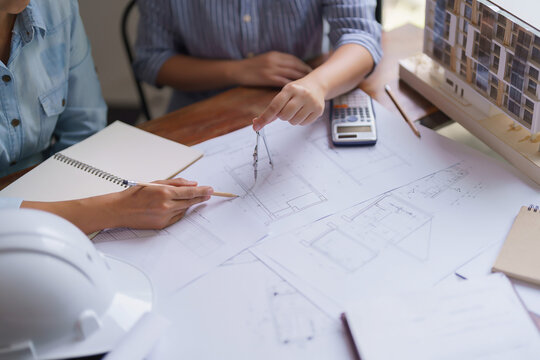 Two architects discuss to designing about building project and using divider compass on blueprint
