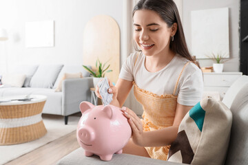 Obraz na płótnie Canvas Female student putting money into piggy bank at home