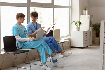 Male medical interns using laptop in clinic hall