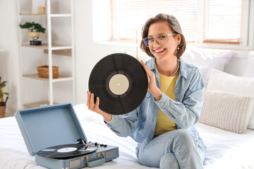 Young woman with vinyl disk and record player sitting in bedroom