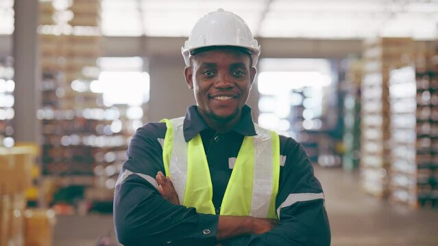 Handsome african man and happy professional worker wearing safety hard hat, Smiling and looking to camera. Big warehouse with shelves full of stock