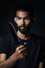 Male killer with beard in a black t-shirt holding a sharp knife on a black background. Dangerous...