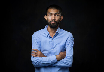 Portrait of young Asian man with beard in a blue shirt with his arms crossed and looking at camera...