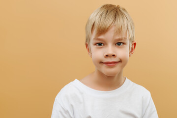 funny kid.handsome little boy.surprised 7 years old child . Kid boy on beige background. Happiness, emotions, smile. The boy is blond. Photo of adorable young happy boy looking at camera.