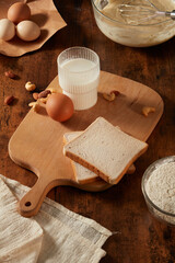 Fototapeta na wymiar A wooden chopping board containing a glass of fresh milk with an egg, nuts and some sandwiches besides, decorated with cream towel and utensils. Blank space for displaying product dairy product 