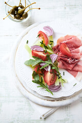Plate of smoked ham with tomatoes and rocket. Bright wooden background. Top view. Copy space.