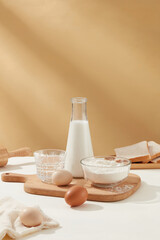 Bowl of flour, eggs and milk bottle featured on wooden chopping board against milk coffee brown...