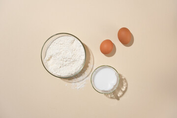 Essential baking ingredients with flour, eggs, and a cup of fresh milk flat lay presenting on the center. Ample empty space for text or adding design elements