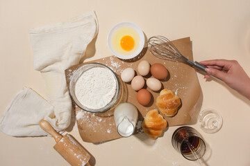 Preparation for baking with several of ingredients and utensils, a female hand is holding a whisk on a vintage paper and decorated with white towel. Photo for cooking layout advertising