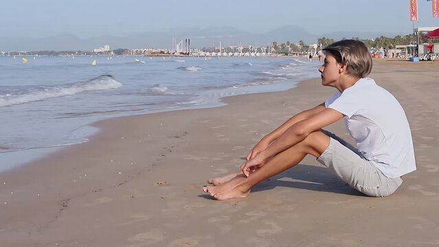Handsome teenager boy sitting at the beach and enjoy a summer vacation.