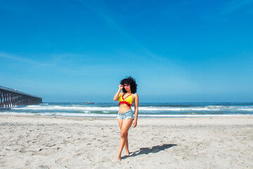 beautiful african american woman on mexican rosarito beach wearing shorts and bikini standing next to pier, latina