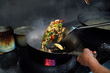 This image showcases the process of stir-frying holy basil (pad krapao) in a sizzling hot wok, a...