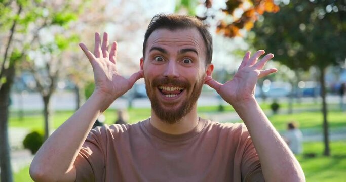 A middle-aged man in the park looks at the camera and makes childish and funny facial expressions