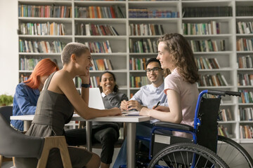 Group of multi-ethnic students and girl with disability engaged in teamwork in high-school library, gathered together for exams preparation, having warm friendly relations. Friendship, communication