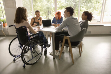 Five diverse students and girl with disability sit at desk in classroom, studying, make exercise,...