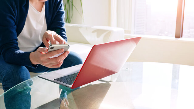 A woman sitting on the sofa and using a smartphone and laptop computer.
