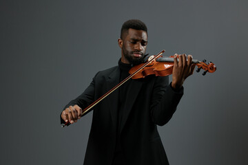 African American male musician in black suit playing violin on neutral gray background, classical...