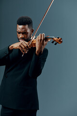 Professional African American violinist in black suit performing classical music on gray background