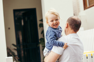 Toddler boy being held by his dad looking towards the camera giggling
