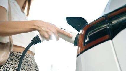 Sunlight backlit brighten young woman travel with EV electric car charging in green sustainable...