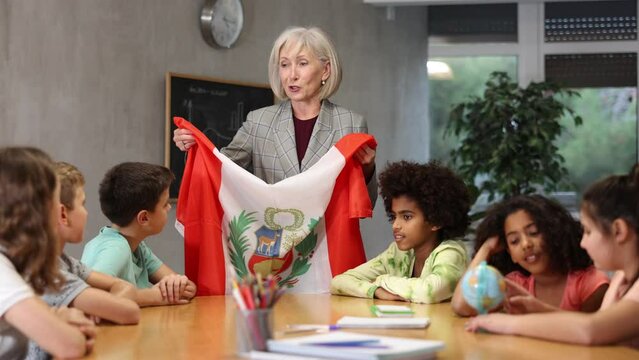 High school woman teacher tells pupils the history of Peru in lesson and holds the national flag of the country in her hands. . High quality 4k footage