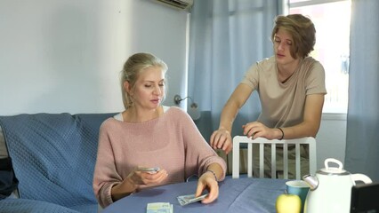 Adult woman sitting at home table counting family budget and holding out pocket money to teenage son . High quality 4k footage