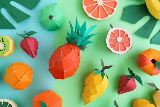 A colorful paper craft arrangement features a variety of fruits on a bright blue background. The scene includes three-dimensional paper art in vibrant colors: a yellow lemon, an orange slice