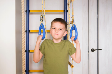 Children's sports. Small active boy hangs on horizontal bar, plays sports at home. Happy childhood. Child is doing pull-ups on horizontal bar. Child development concept.