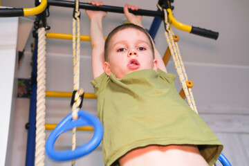 Children's sports. Small active boy hangs on horizontal bar, plays sports at home. Happy childhood. Child is doing pull-ups on horizontal bar. Child development concept.