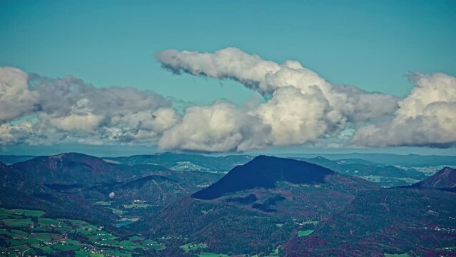 Fluffy white clouds roll and curve in sky above rugged mountain peaks in countryside