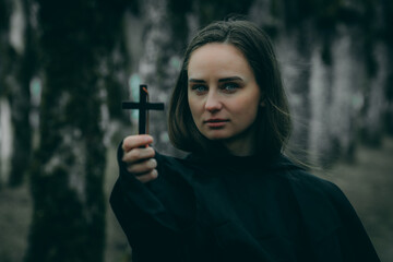 A woman in a black cloak holds a black cross