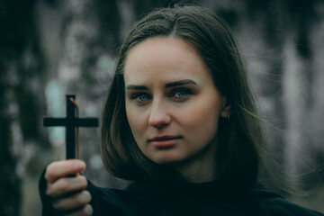 A woman in a black cloak holds a black cross