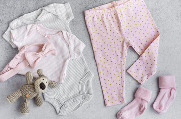 Set of baby bodysuits, pants, socks and knitted toy on grey background.