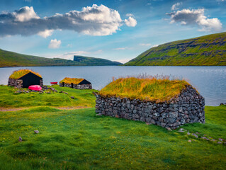 Spectacular summer view of typical turf-top houses and red fishing boat on the sopre of Sorvagsvatn lake, Vagar island. Wonderful morning view of Faroe Islands, Kingdom of Denmark, Europe. - 784987710