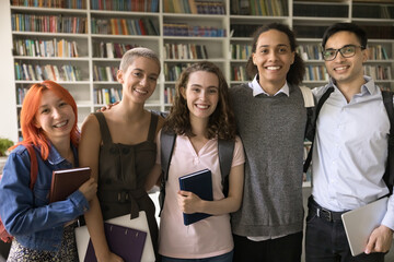 Five smiling attractive multiethnic schoolmates posing, standing in row gathered in college or...