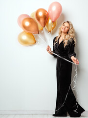 Beautiful Woman with Balloons over White background. Birthday Party Time. Fashion Model with Curly Hairstyle in Black Long Dress - 784997941