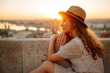 Portrait of female tourist looking at panoramic view of the city at sunset. Lifestyle, travel, tourism, nature, active life. - obrazy, fototapety, plakaty