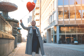middle-aged happy woman with a heart-shaped balloon falling a love, having a fun day, walking...