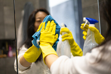 Cleaning service concept. Close up of female hands in yellow gloves cleaning mirror