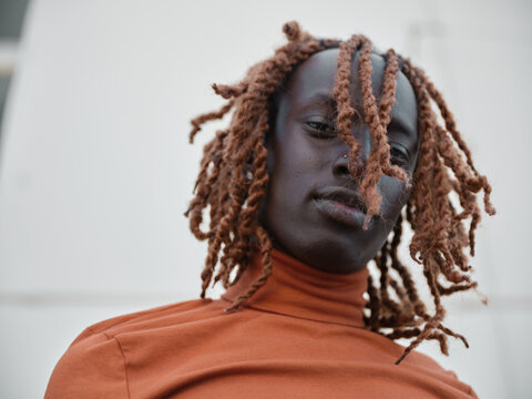 South Sudanese man wearing orange turtleneck looking down