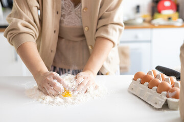 cropped shot of woman preparing dough with flour and egg on kitchen table. Woman preparing...