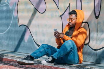 urban afro woman sitting on graffiti wall with mobile phone