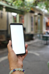  holding smart phone with empty screen with blurred cafe street background.
