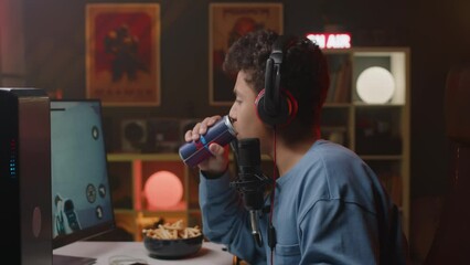 Side view waist up shot of Biracial teenage boy in headset playing online first person shooter game on personal computer in neon light room in apartment at nighttime