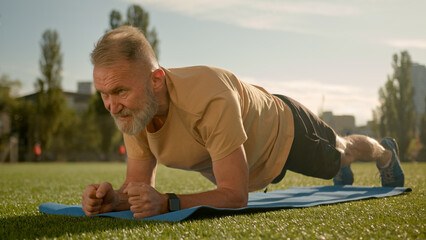 Caucasian old man in plank exercise workout training stadium city outside effort strain fitness...