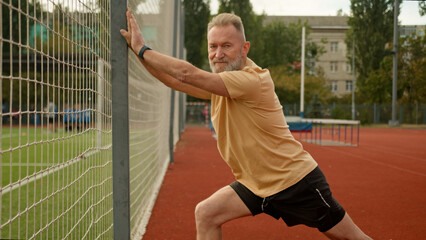 Elderly Caucasian man pensioner athlete outside city stadium physical activity sport flexibility...